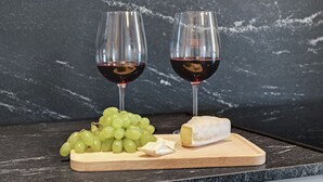 Two glasses of red wine, a bunch of green grapes, and a piece of cheese on a wooden board. - Lion Apartments - City Center (Gdansk)