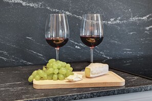 Two glasses of red wine, a bunch of green grapes, and a piece of cheese on a wooden board. - Lion Apartments - City Center (Gdansk)
