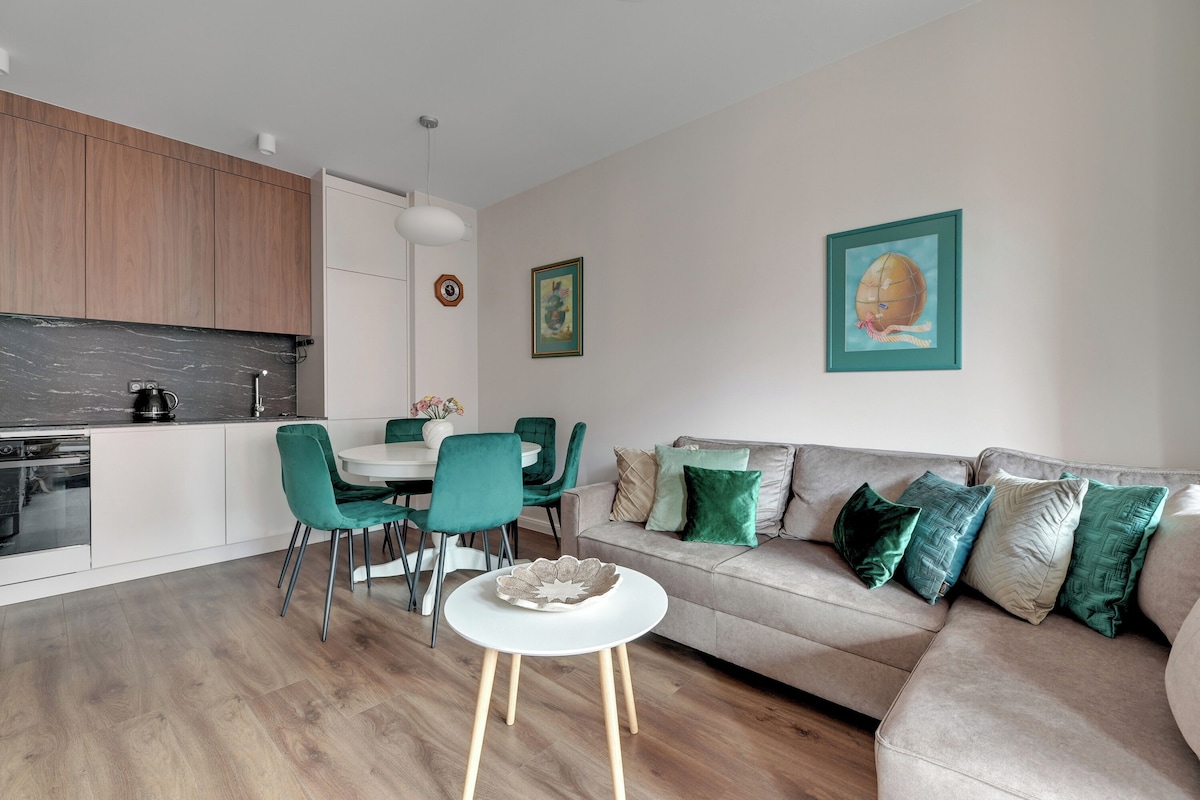 A modern kitchen with a dining area, a sofa with green cushions, and a small white table.