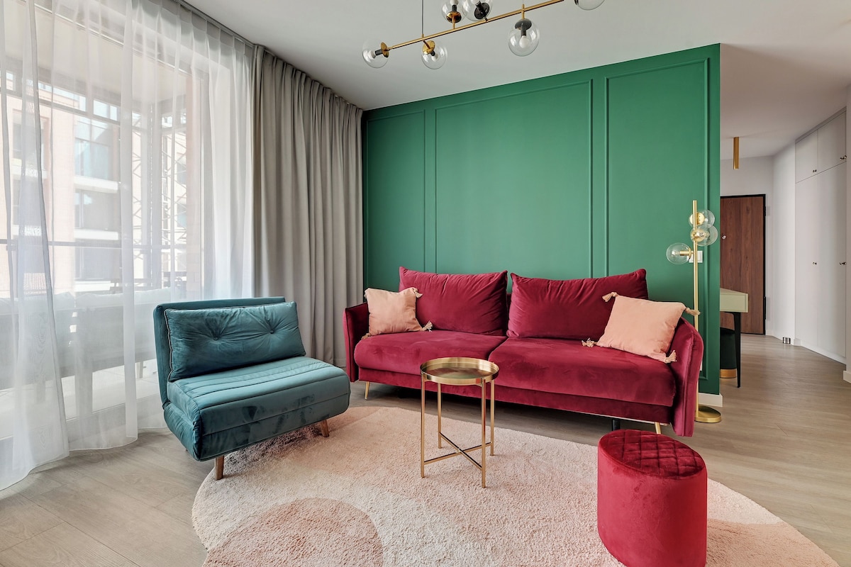 A modern living room with a teal sofa, a red sofa, a small round table, and a red ottoman.