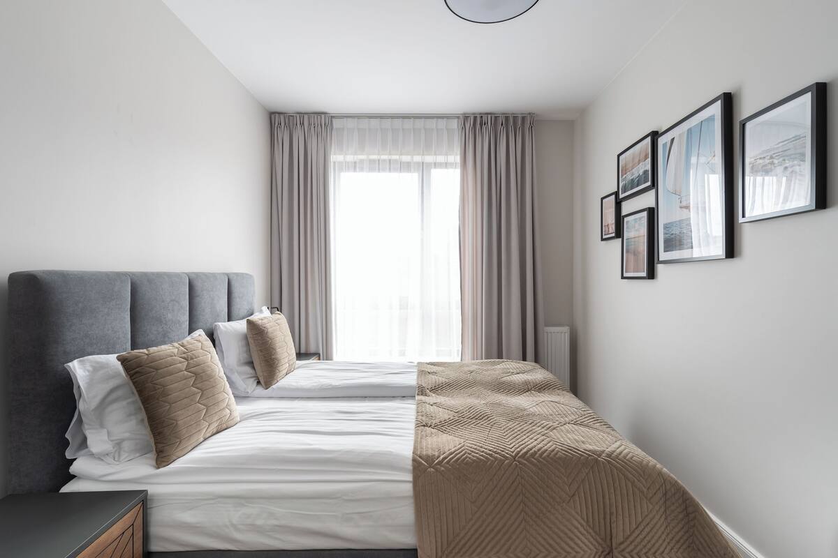 A modern bedroom with a bed, a bedside table, and a large window with curtains.