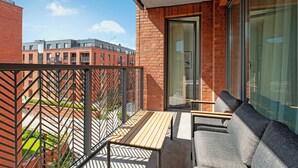 A balcony with a wooden table and grey sofa, overlooking a brick building and greenery. - Lion Apartments - City Center (Gdansk)