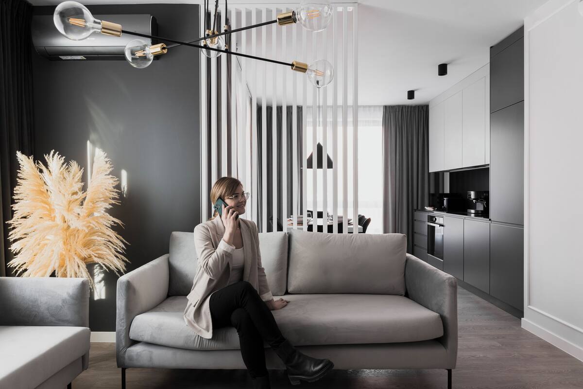 A modern living room with a grey sofa, a tall vase with pampas grass, and a kitchen in the background.