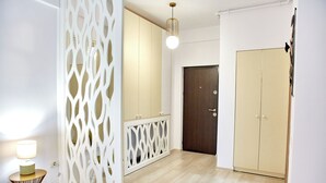 Un interior moderno con piso de madera, un armario color beige, una puerta oscura y un separador blanco decorativo.