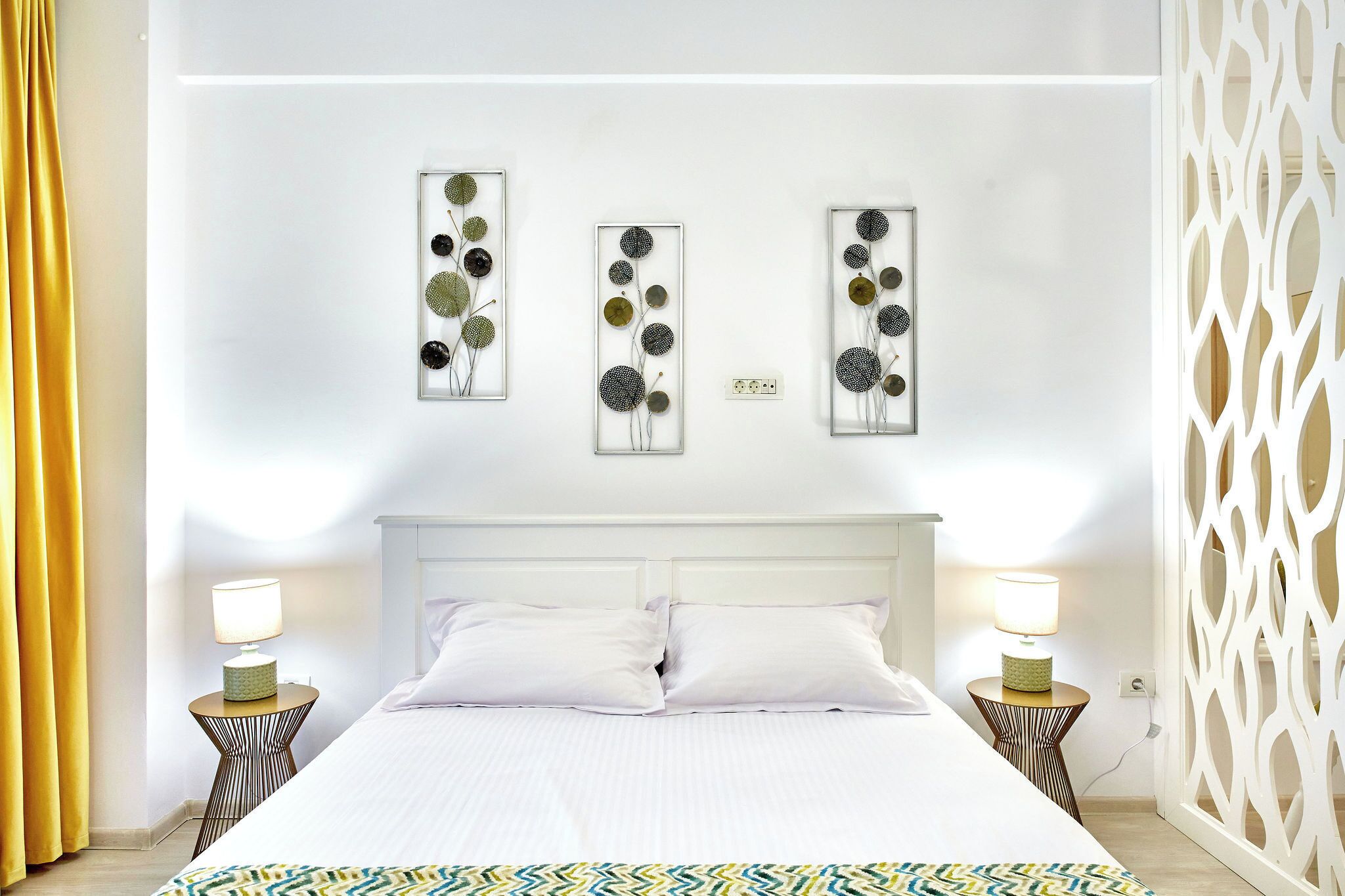 Una habitación de hotel con una cama, dos mesitas de noche con lámparas y tres obras de arte colgadas en la pared.