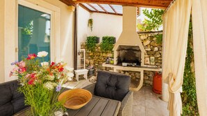 An outdoor patio with a stone wall, a wooden ceiling, and a barbecue grill. - Casa Vito in Žužići  - Haus für 4 Personen (Višnjan)