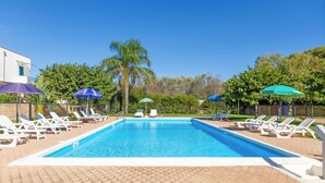 Une piscine rectangulaire à l’eau d’un bleu cristallin, entourée de chaises longues blanches et de parasols.
