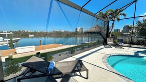 Un espace piscine avec vue sur un plan d’eau, une chaise longue et une petite table.