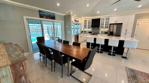 Une cuisine moderne avec des meubles blancs, un îlot central doté de tabourets de bar et un coin repas avec une table et des chaises en bois.
