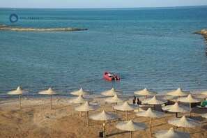 A beach with umbrellas and a boat in the water. - Beachfront Stay - Pool - Balcony - Central (Hurghada)