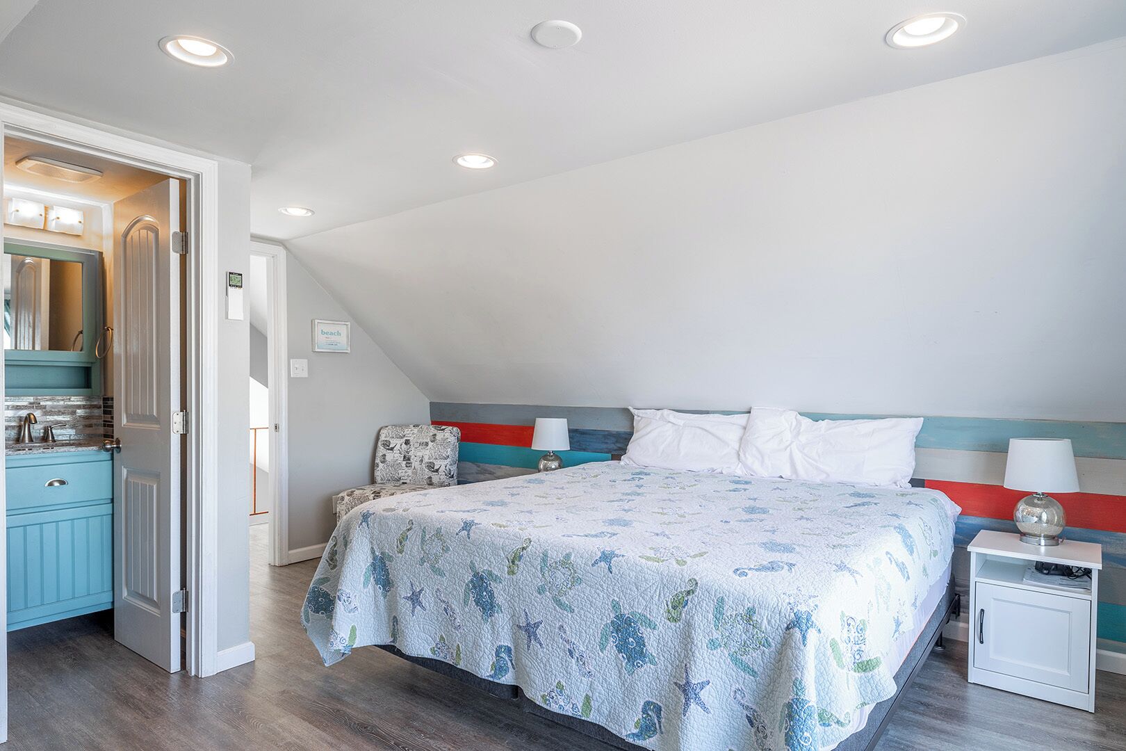 A bedroom with a bed, bedside tables, a nightstand, a dresser, and a door leading to another room.
