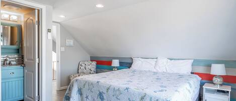 A bedroom with a bed, bedside tables, a nightstand, a dresser, and a door leading to another room.