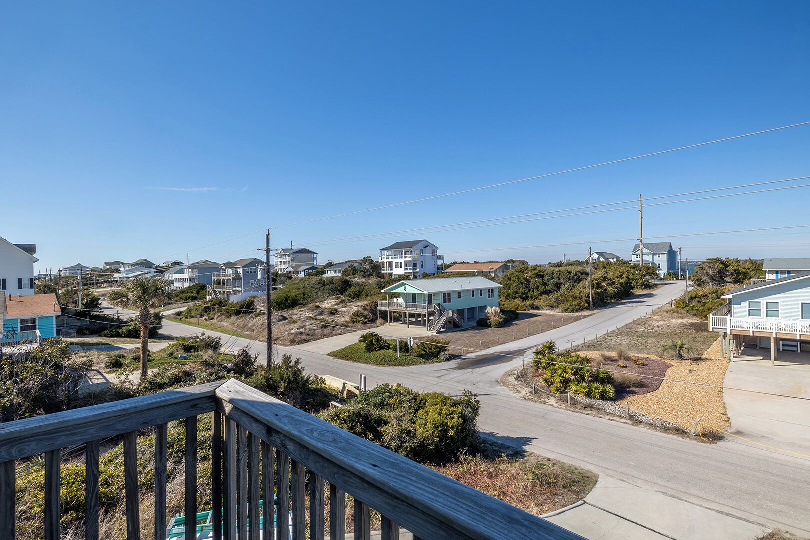 Uma área residencial à beira-mar, com casas, céu claro e um deck de madeira em primeiro plano.