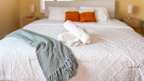 Una cama bien hecha con edredón blanco, dos almohadas y una toalla doblada.