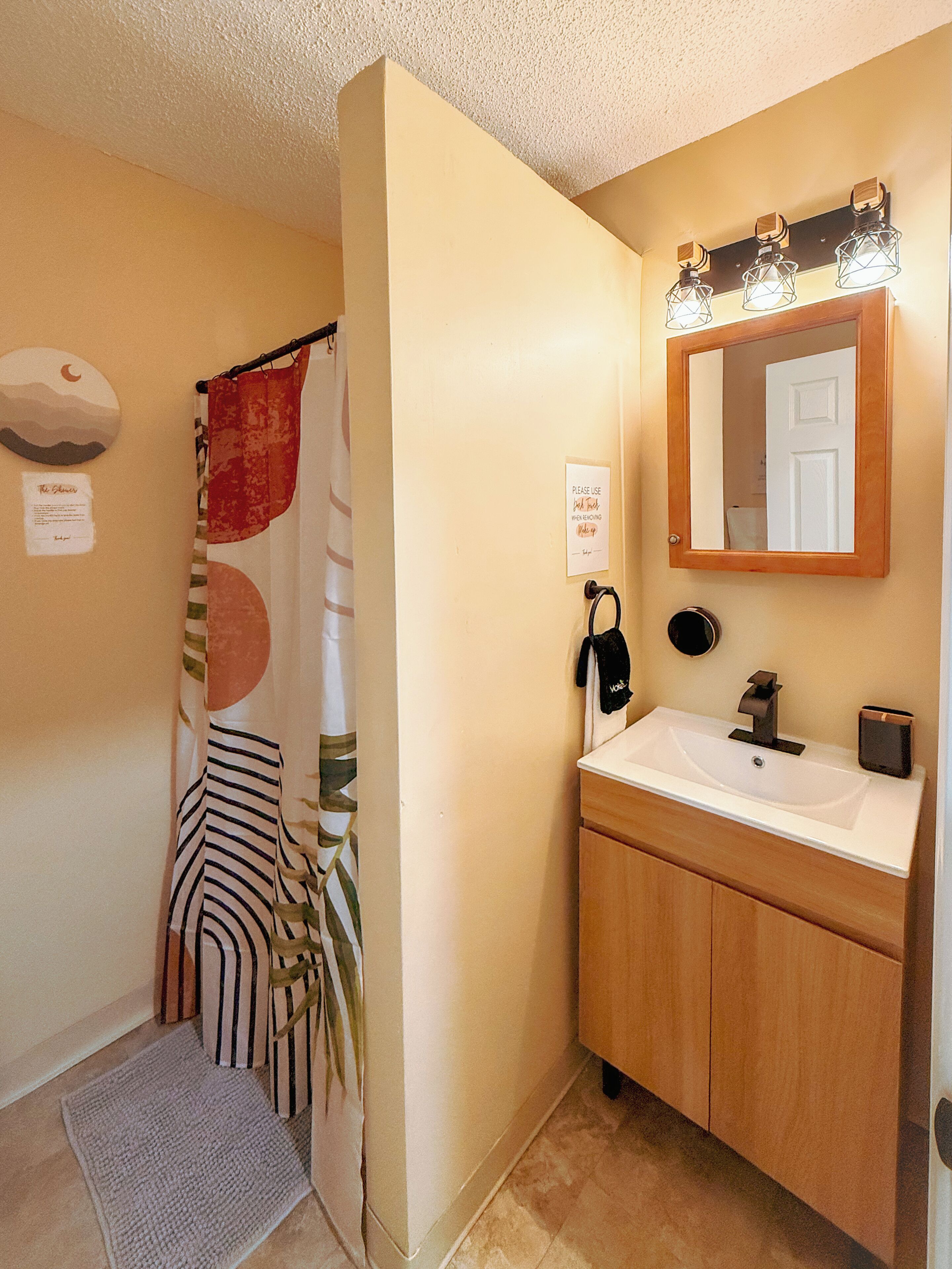 Une salle de bain avec un rideau de douche, un lavabo, un miroir et un porte-serviettes.