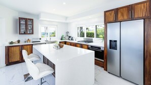 A modern kitchen with a large island, wooden cabinets, stainless steel appliances, and a view of greenery outside. - 360 views Ocean and Jungle villa in amazing Ocotal! Enjoy the paradise! (Guanacaste province)