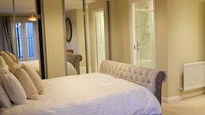 Une chambre à coucher avec un grand lit, un miroir, une armoire et une porte donnant sur une salle de bain.