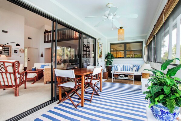 A modern living room with a dining area, large windows, and a ceiling fan.