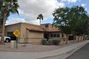 A building with a 'Not a thru street' sign, a garage, and a small front yard with a palm tree and shrubs.