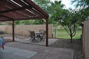 A covered patio area with a table and chairs, surrounded by a brick wall and a grassy field.