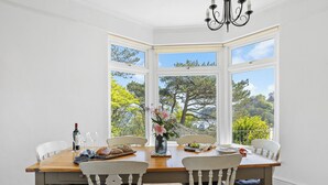 A dining area with a bay window, wooden table, white chairs, and a chandelier. - Moult Sylvan, Homely 4 bed, stunning sea views, Salcombe (Salcombe)