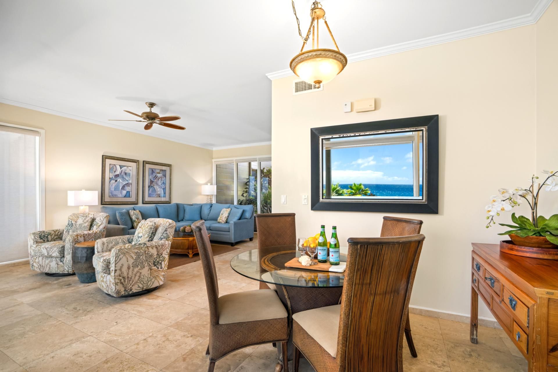 A spacious living room with a blue sofa, patterned armchairs, a glass coffee table, and a wooden sideboard.