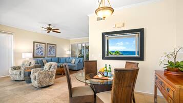 A spacious living room with a blue sofa, patterned armchairs, a glass coffee table, and a wooden sideboard.
