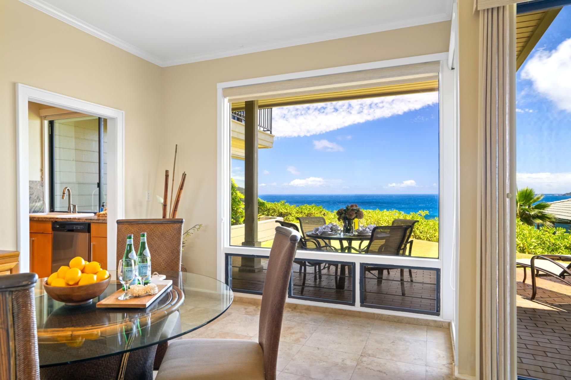 A balcony with a view of the ocean, a dining table with chairs, and a kitchen area with a sink and a bowl of lemons.