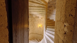 A spiral staircase in a stone-walled room with a wooden door and a wall-mounted light fixture. - Château de Goudourville 13th century, private, sleeps 30, swimming pool, reception area (Goudourville)
