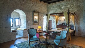 A bedroom with a four-poster bed, a sitting area with a table and chairs, and a view through an arched window. - Château de Goudourville 13th century, private, sleeps 30, swimming pool, reception area (Goudourville)