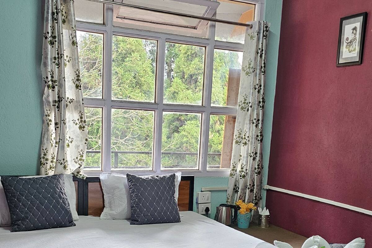 Un dormitorio con una cama grande, una ventana con cortinas, una pared roja y un cuadro enmarcado.