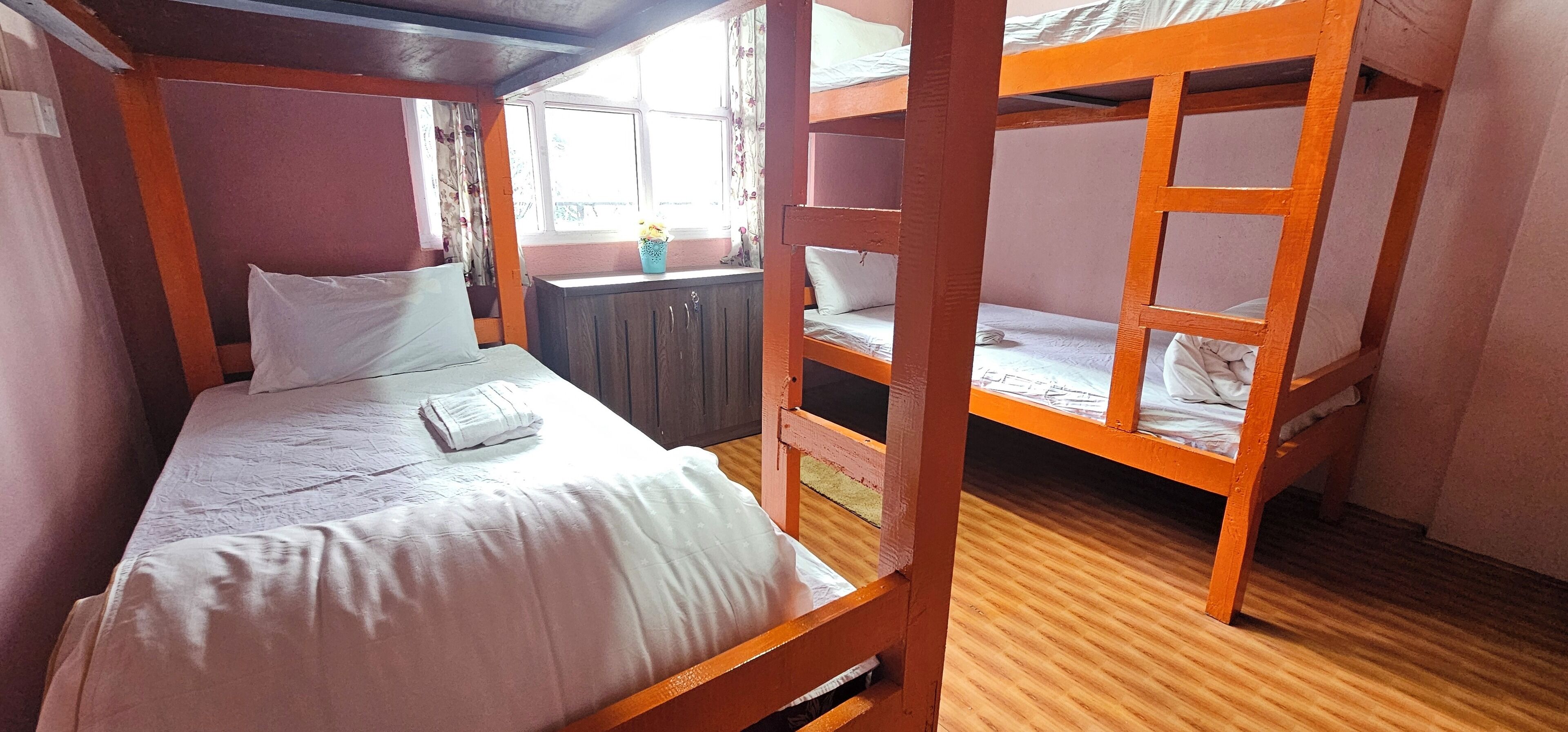 A bunk bed room with a window, wooden floor, and a small table with a vase.