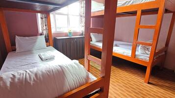 A bunk bed room with a window, wooden floor, and a small table with a vase.