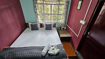 A neatly made bed with pillows and a quilted blanket, a small table with a vase of flowers, and a window with curtains.