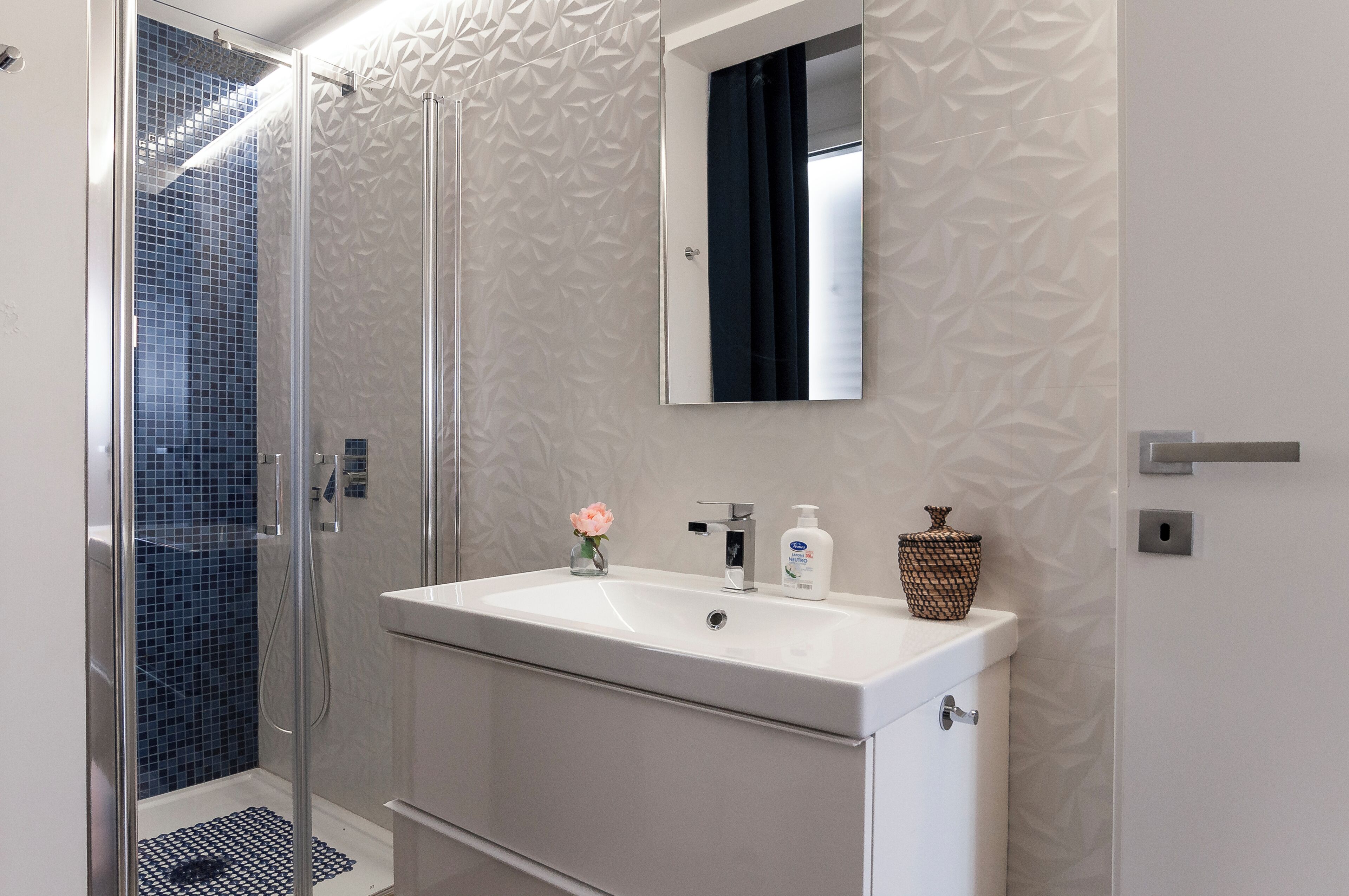 A bathroom with a white sink, a mirror, and a shower with blue tiles.