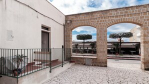 Um pátio com um arco de pedra, plantas em vasos e piso de azulejos.