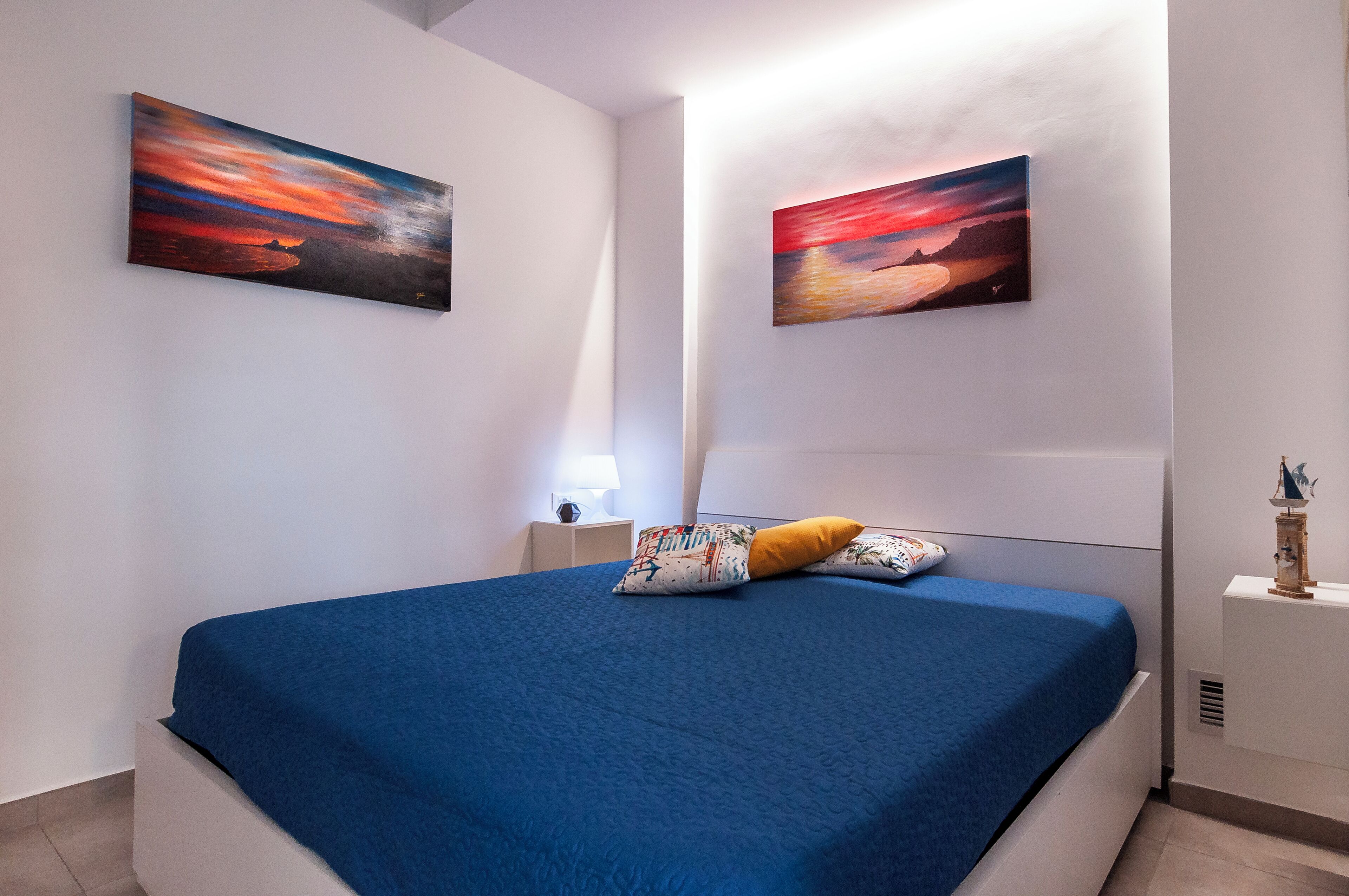 Une chambre à coucher avec un lit, deux tableaux accrochés au mur, une table de chevet et une lampe.