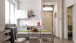 Cozinha moderna com armários brancos, coifa de aço inoxidável e área de jantar com mesa posta para quatro pessoas.