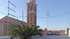 Une terrasse sur le toit, agrémentée de plantes en pot, une table avec des boissons et des amuse-gueules, et une vue sur une tour en arrière-plan.