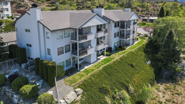 A multi-story residential building with balconies, a landscaped garden, and a hilly backdrop. - Park Pointe B102 – Walk to the Beach & Enjoy the Pool & Hot Tub! (Chelan)