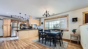 Una cocina moderna con armarios de madera, un refrigerador de acero inoxidable, una mesa de comedor con sillas y una araña.