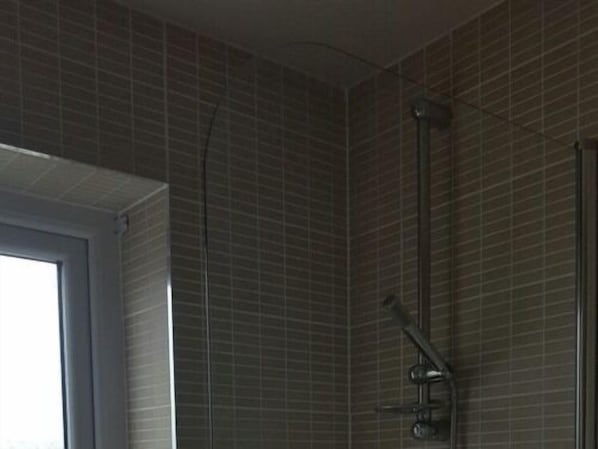 A bathroom with a shower, tiled walls, and a window. - A35 PitStop (Axminster)