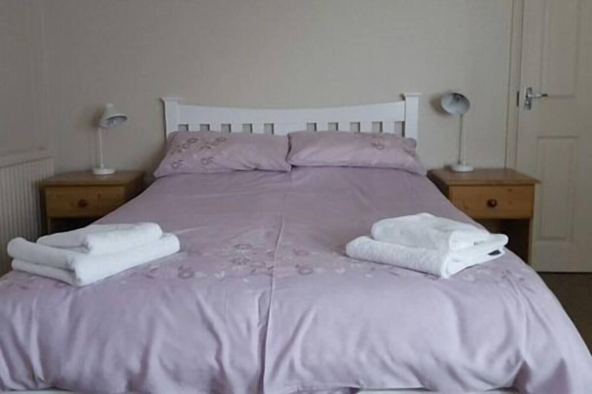 A neatly made bed with a white headboard, two bedside lamps, and a door in the background.