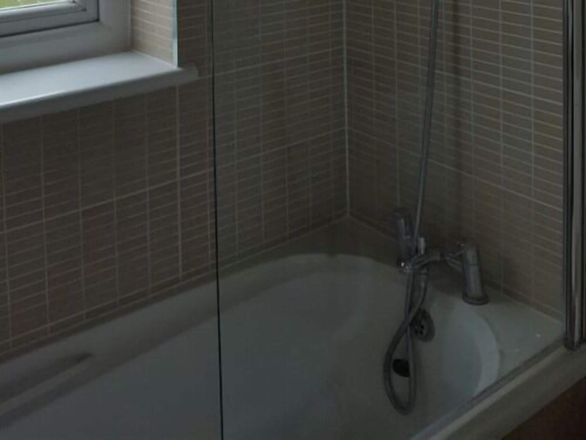 A glass-enclosed shower with a bathtub, tiled walls, and a window above the tub.