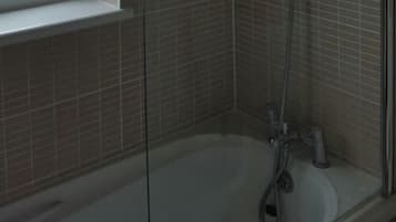A glass-enclosed shower with a bathtub, tiled walls, and a window above the tub.