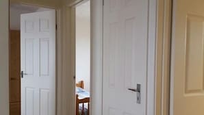 A hallway with white doors, one of which leads to a room with a bed and a wooden chair. - A35 PitStop (Axminster)