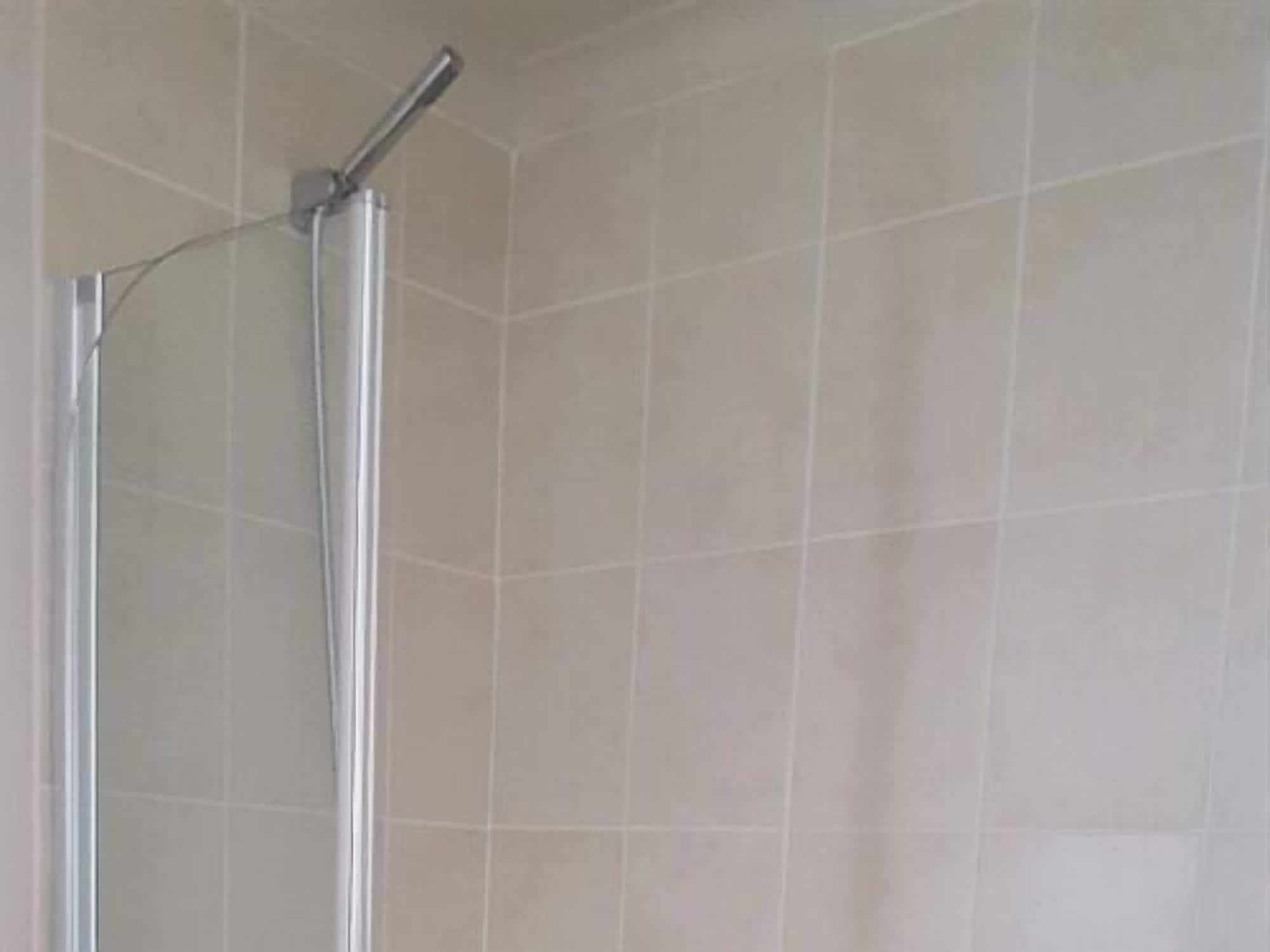 Een douche met een chroomhendel en een glazen deur, in een betegelde badkamer.