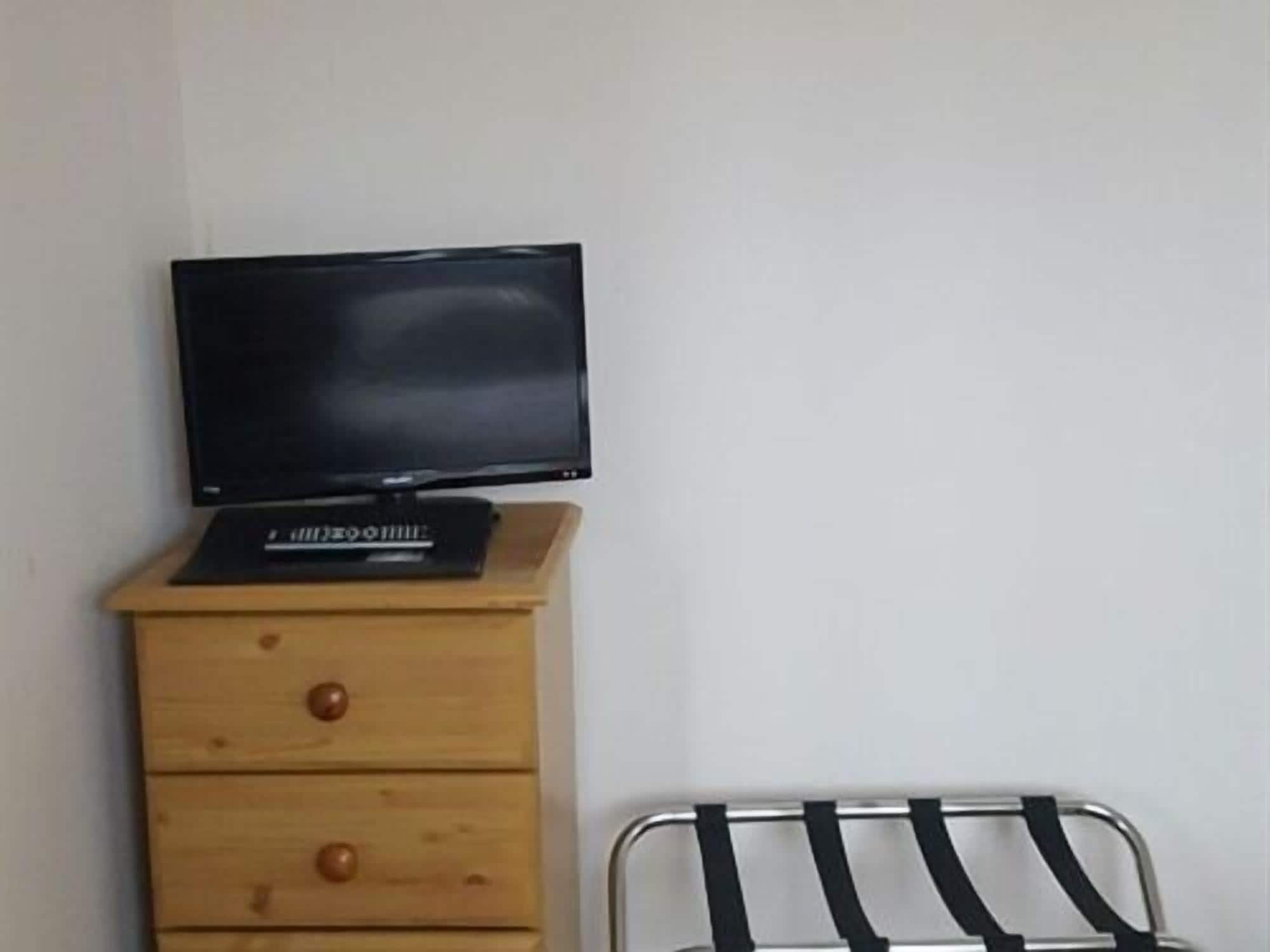 A room with a wooden dresser, a television on top, and a metal chair with a black seat.
