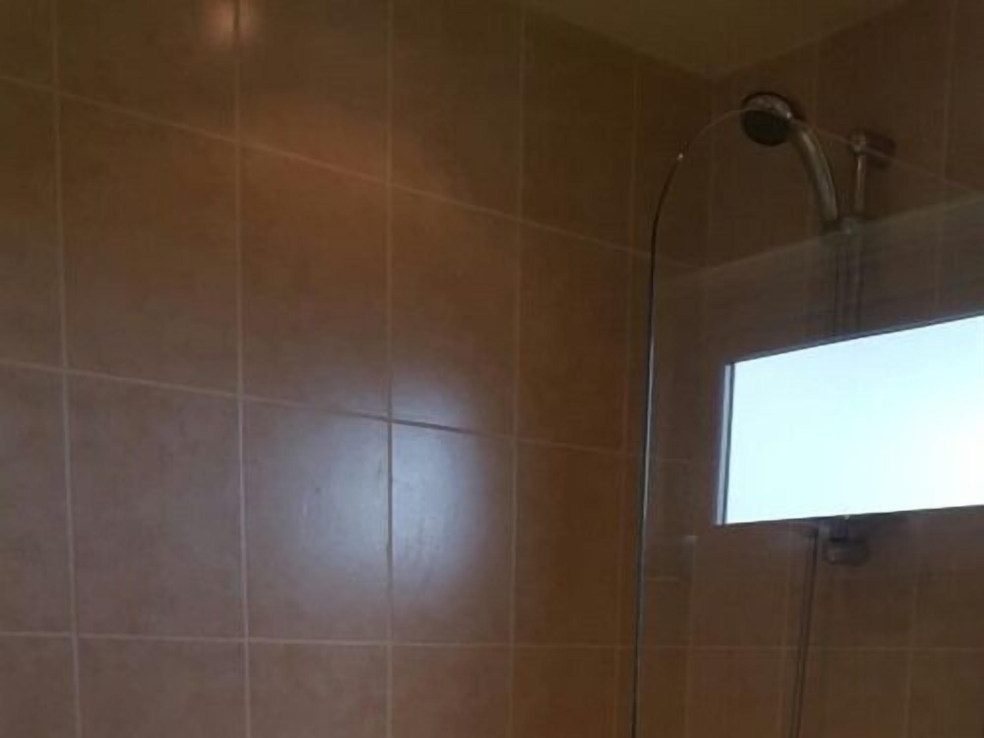 A bathroom with brown tiles, a shower, and a window.