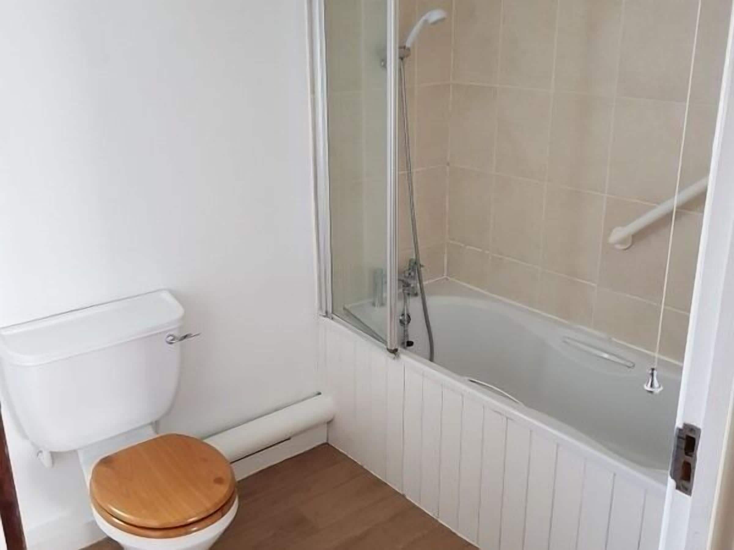 A small bathroom with a toilet, a shower enclosure, and a wooden floor.